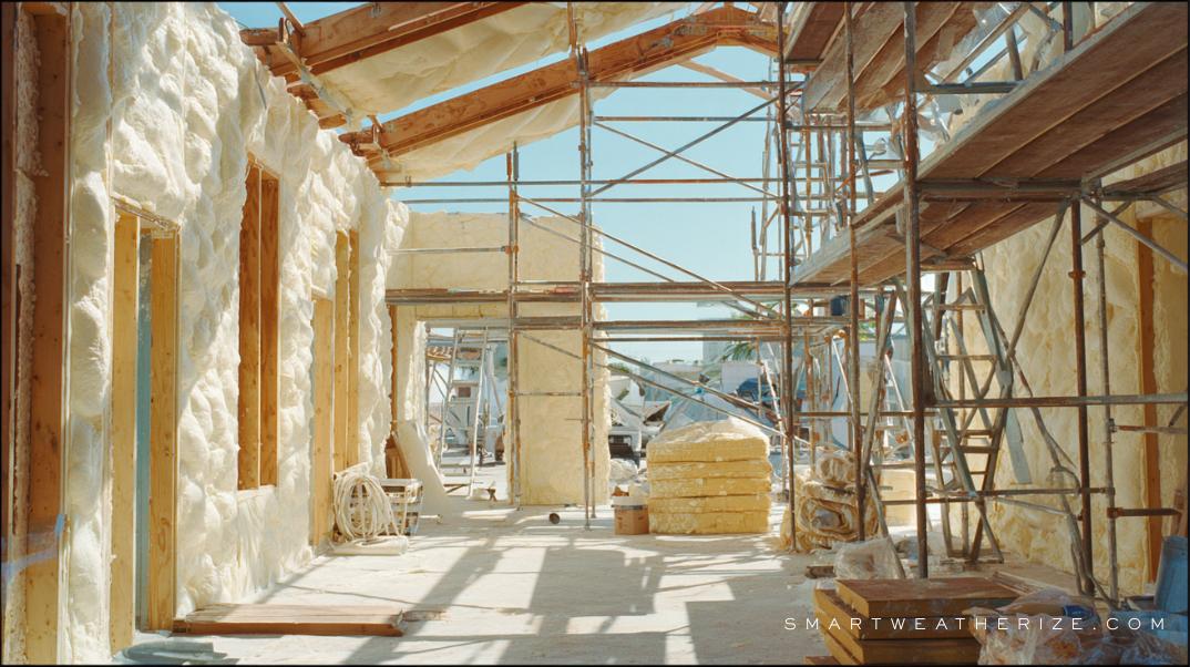 Workers applying spray foam and rigid board insulation on a commercial building